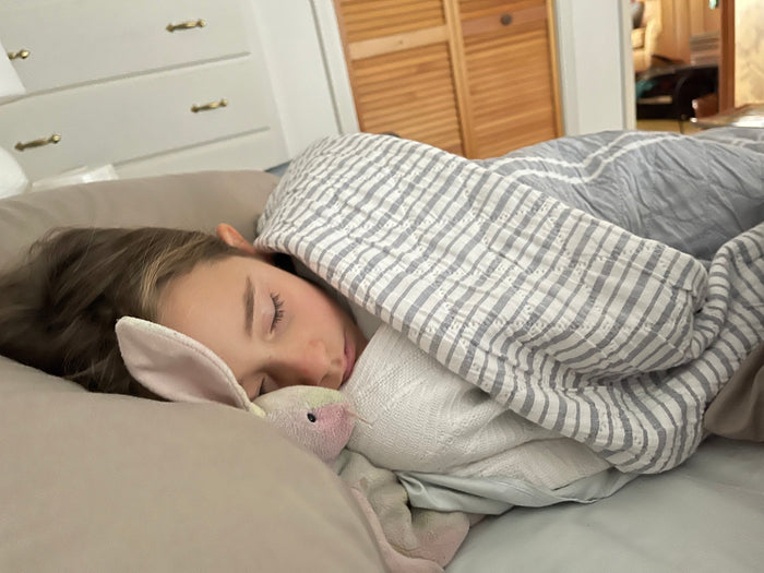 Sleeping girl, snuggling with stuffed bunny and covered in striped blanket